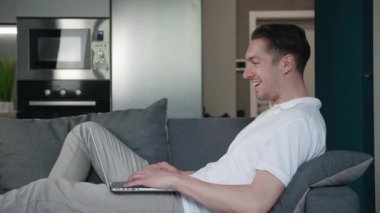 Mutlu genç adam başarıyı kutluyor online bahsi kazanıyor ve EVET hareketi gösteriyor. Şanslı erkek serbest yazar internette harika haberler okuyor. Evdeki rahat koltukta dinlenirken dizüstü bilgisayar kullanıyor..