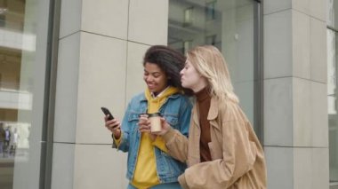 Şehir caddesinde yürürken akıllı telefon kullanan, gülen ve akıllı telefondan bir şeyler izleyen iki farklı çekici bayan arkadaş..