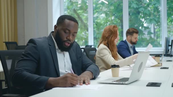 Der geschäftige afrikanische Geschäftsmann hat eine Online-Videokonferenz auf seinem Laptop, kommuniziert aus der Ferne, diskutiert Fälle und macht sich Notizen. Männlich mitarbeiter mit ein video anruf auf laptop während der arbeit im büro. — Stockvideo