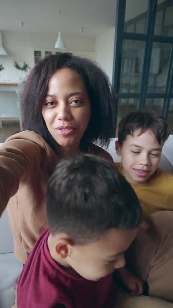 Збільшений вертикальний відеопортрет щасливої афро-американської жінки, яка тримає мобільний телефон у витягнутих руках, ніжно обіймаючи своїх чарівних синів і дивлячись на веб-камеру під час відеодзвінка.. — стокове відео