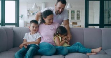 Mutlu bir Afrikalı Amerikalı kadın, bir oğlan ve bir kız çocuğuna nazikçe sarılıp öpüyor, kanepede dinleniyor, ve sevgili kocası onlara yaklaşıyor ve nazikçe ailesine sarılıyor. 4K video