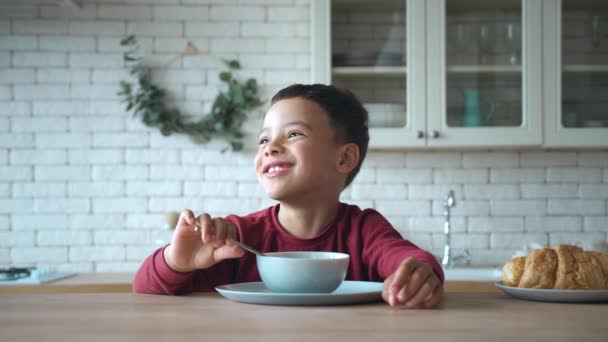 クローズアップ肖像画。台所のテーブルに座っている間、就学前の男の子は朝食のためのおいしい甘いチョコレートシリアルを楽しんでいます。健康的な朝食を取る愛らしい子供。朝のルーチン国内生活 — ストック動画