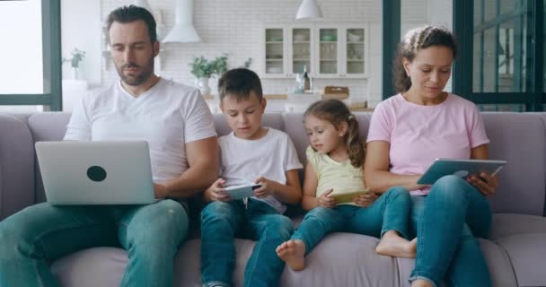 Il video 4K dei membri della famiglia si è concentrato sul lavoro sul dispositivo digitale personale. Giovane padre freelance che lavora su laptop, madre su tablet digitale e bambini carini seduti tra i loro genitori impegnati — Video Stock