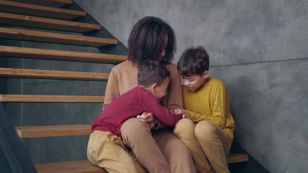 Jucăușă rasă mixtă etnie copii, răsfățându-se împreună, așezat pe scări în laturile mamei lor vesele. Fiii se joacă cu mama lor. Relații de familie fericite, copilărie fără griji . — Videoclip de stoc