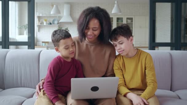 Jeune maman assise près de ses fils, surfant sur un ordinateur portable, faisant des achats en ligne sur des sites Web, faisant du shopping, réservant des destinations de voyage, parlant aux tout-petits. Famille de trois liens s'amuser ensemble — Video