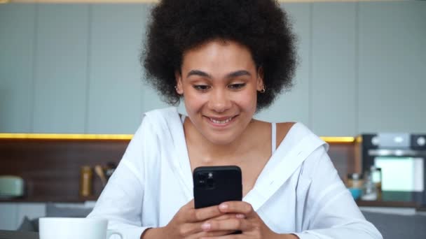 Primer plano de una hermosa joven mestiza, escribiendo con entusiasmo texto en su smartphone, sonriendo de felicidad. Retrato de una hermosa chica afroamericana divirtiéndose en el teléfono celular — Vídeo de stock