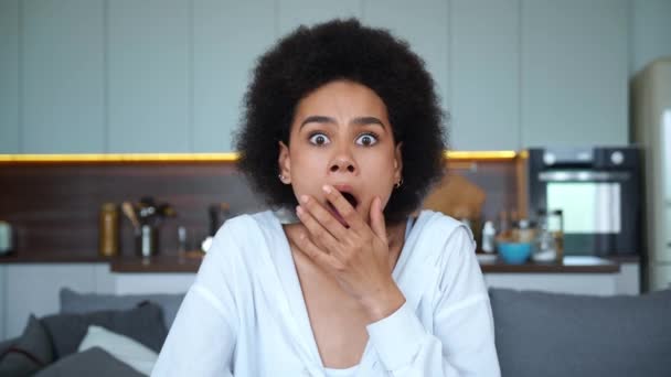 Närbild porträtt. Ung afroamerikansk kvinna tittar rakt in i kameran, uttrycker känslor av fasa över att få dåliga nyheter, täcker munnen och håller sina tempel med handen — Stockvideo