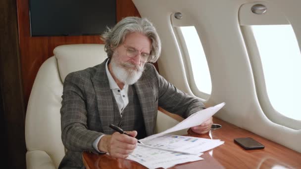 Ocupat suprasolicitat barbă om de afaceri matur obosit de a lucra cu laptop și documente de hârtie, își scoate ochelarii și se întinde pe un scaun în avion privat sau primul avion de clasă business — Videoclip de stoc