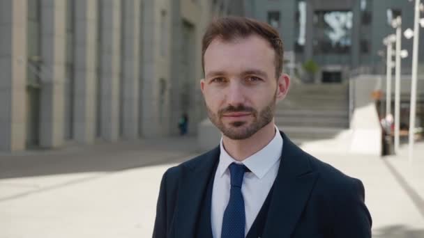 Retrato de un ejecutivo sonriente mirando a la cámara. Hombre de negocios en los años 30 con traje clásico posando al aire libre en el fondo moderno edificio de oficinas — Vídeos de Stock