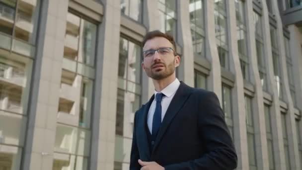 Portrait bel homme d'affaires en lunettes marchant à l'extérieur près de l'immeuble de bureaux. Homme en costume formel regardant loin à l'extérieur de la ville — Video