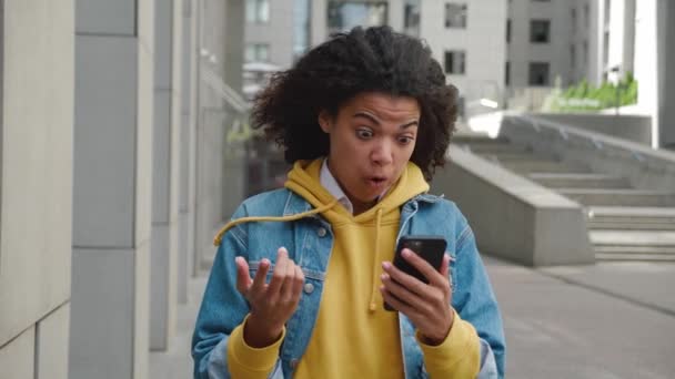 Joven mujer de raza mixta mantenga teléfono inteligente leer sms desagradables, frustrado por las noticias recibidas horribles se siente molesto mientras está de pie al aire libre en la calle de la ciudad — Vídeo de stock