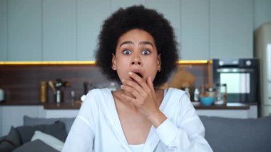Ekran kamerasına doğrudan bakan melez bir Afrikalı Amerikalı kadının yakın plan portresi. Ağzını eliyle kapatıyor. Korku, şaşkınlık, hayal kırıklığı ve hayal kırıklığını ifade ediyor.