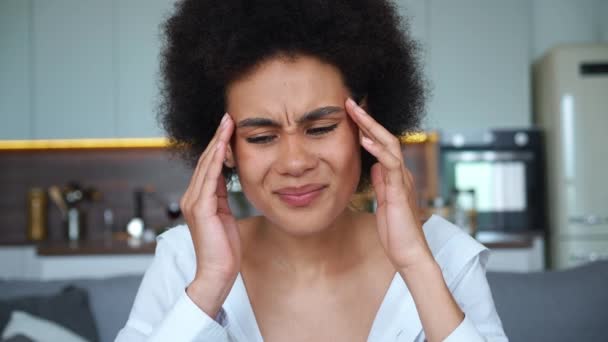 Retrato facial de perto de uma jovem mulher afro-americana atraente tocando seus templos, sofrendo de enxaqueca, sentindo-se doente por causa de uma terrível dor de cabeça. Mulher perturbada que sofre de espasmos na cabeça — Vídeo de Stock