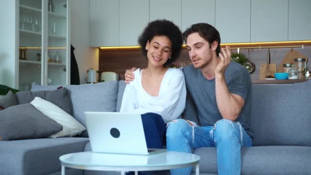Adorable couple makes video call via mobile application on laptop. Handsome guy gently hugs his girlfriend, introduces her to interlocutor, pressing cheek to cheek , showing love tenderness affection — Stock Video