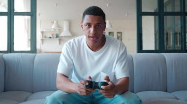 Dijital bağımlı, endişeli Afrikalı bir adam monitör önünde bilgisayar oyunları oynuyor, joystick 'e basıyor, seviniyor ve kaybettikten sonra üzülüyor, oyun çubuğunu kafasına geçirip hayal kırıklığına uğruyor.