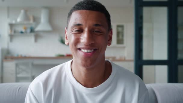 Portrett av en kjekk afroamerikansk blandingsrase som gjemmer seg hjemme og smiler mens han stiller seg foran kamera. Fokuser på det rolige utseendet til en ung mann med toothy smil, ser fortrolig inn i kameraet – stockvideo