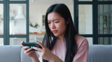 Akıllı telefonda sanal bilgisayar oyunları oynayan heyecanlı bir Asyalı kadının yakın plan portresi zaferin tadını çıkarıyor, yazı yazıyor ve dokunmatik ekrana bakıyor, dişlek gülümsüyor. Bilgisayar Sanal Oyun Bağımlılığı