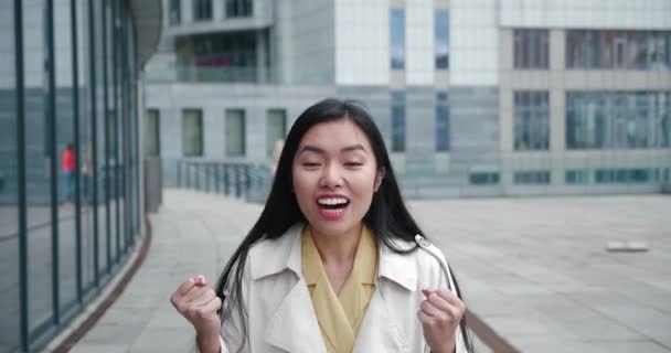 Entusiasta emocionado feliz joven asiática levantando puño en gesto victorioso, bailando gritando Sí lo hice, celebrando un gran éxito, disfrutando de un día de suerte, de pie al aire libre en el centro de distrito — Vídeo de stock