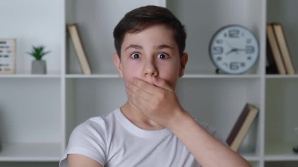 Portret przerażonego chłopca wstrząśnięty okropną sceną, przerażony nastolatek patrzący w kamerę, zakrywający usta dłonią w domu. — Wideo stockowe