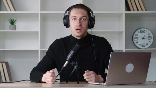 Šťastný mladý muž audio blogger ve sluchátkách vysílání na mikrofon ve studiu. Koncept podcastu — Stock video