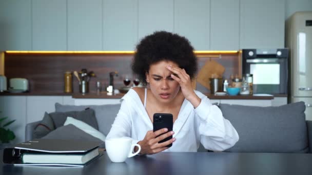 A fiatal afro-amerikai nő rémült, csalódott amiatt, amit a kezében lévő mobiltelefon képernyőjén olvasott vagy látott. Gyönyörű fiatal hölgy aggódik a rossz hírek miatt. Zaklatott és zavarodott érzelmek. — Stock videók