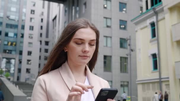 Πορτρέτο της εμπιστοσύνης των γυναικών των επιχειρήσεων δακτυλογράφηση από κινητό τηλέφωνο, ενώ το περπάτημα σε εξωτερικούς χώρους στο δρόμο της πόλης. Κοντινό πλάνο γυναίκα διευθυντής χρησιμοποιώντας smartphone, ενώ πρόκειται να εργαστούν. Σφηνάκι Steadicam. — Αρχείο Βίντεο