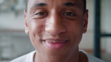 Yakın plan. Kameraya poz verirken gülümseyen yakışıklı Afro-Amerikan bir adamın kendinden emin portresi. Dişleriyle gülümseyen ve kameraya özgüvenle bakan genç bir adamın sakin bakışına odaklan.