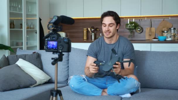 Attraktiv stilig kille frilansare bloggare i casual denim spelar in video med kamera på ett stativ, håller drönare quadcopter och presenterar den för kameran, beskriver dess egenskaper och egenskaper — Stockvideo