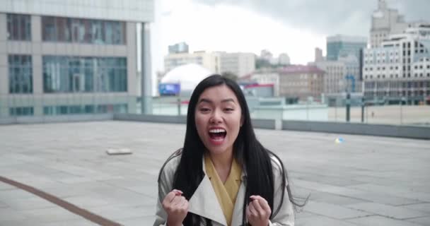 Entusiasta emocionado feliz joven asiática levantando puño en gesto victorioso, bailando gritando Sí lo hice, celebrando un gran éxito, disfrutando de un día de suerte, de pie al aire libre en el centro de distrito — Vídeo de stock