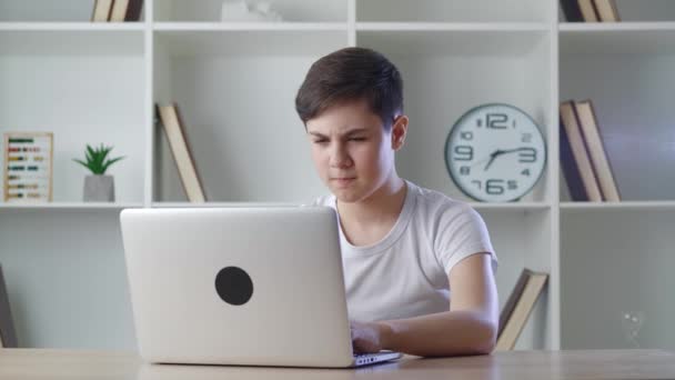 Счастливый мальчик 13 лет радуется достижениям, работающим дома за компьютером, показывая знак "да". Подросток приятно удивлен внезапной победой, играя со своим ноутбуком. — стоковое видео