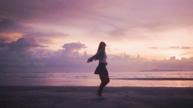 Kollarını açıp plajda tropikal pembe günbatımının tadını çıkaran mutlu genç kadın tropik cennet kumsal tatili ve güzel gün batımının keyfini çıkarıyor. Mutluluk kavramı