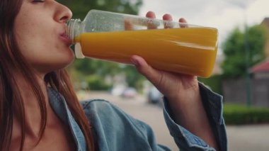 Soğuk turuncu içecekten hoşlanan odaklanmış bir kadın, posalı narenciye suyu içen bir kadın, dokuma sıvısıyla taze portakal suyu içen bir kadının görüntüsü.