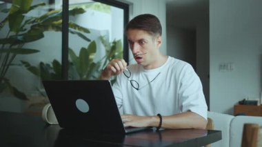 Evde dizüstü bilgisayarda çalışan Millennial 'lı bir adam, sürpriz şok ve stresle tepki veriyor. Yurtiçi ofisteki serbest çalışan genç adam, internette kötü haberlerle karşılaşıyor.