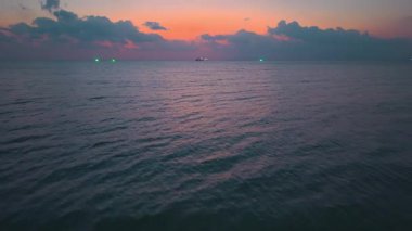 Güzel pembe bir günbatımının sinematik görüntüsü, denizin üzerinde uçan bir dronun açılış sahnesi, denizin üzerinde güzel bir kızıl gün batımı, uzaklarda seyreden bir gemi. Okyanusun üzerinde renkli gün batımı