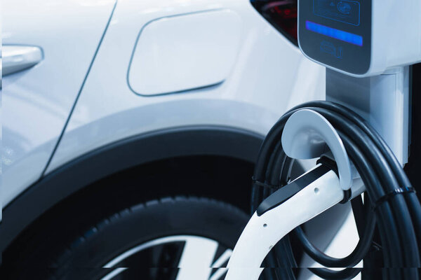 Close-up of an electric vehicle charging port and power cable plugged into a modern white car at a charging station.