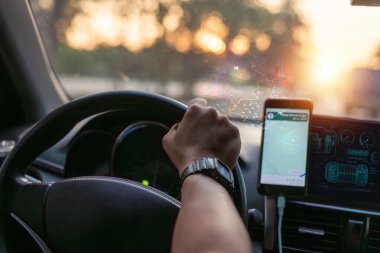 Günbatımında araba kullanan kişi, gerçek zamanlı yol gösterimi ve seyahat yönü için gösterge panelinde akıllı telefon GPS navigasyon uygulaması kullanıyor..