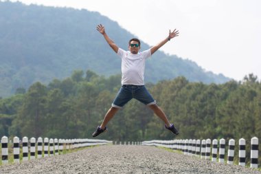Uzun boylu, güneş gözlüklü mutlu Asyalı bir adam doğa kökenli bir şekilde yola atlıyor. Özgürlük, seyahat, tatil ve hayattan zevk alma kavramı.