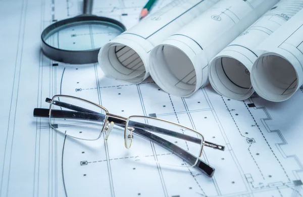 Architectural blueprints and blueprint rolls and a drawing instruments on the worktable — Stock Photo, Image