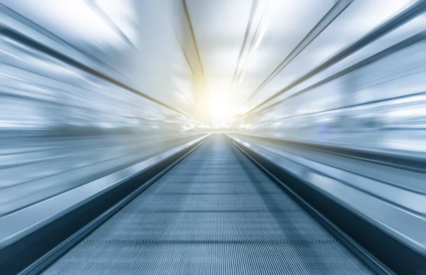 Perspective wide angle black and white view of modern light blue illuminated and spacious high-speed moving escalator with fast blurred trail of handrail in vanishing traffic motion — Stock Photo, Image