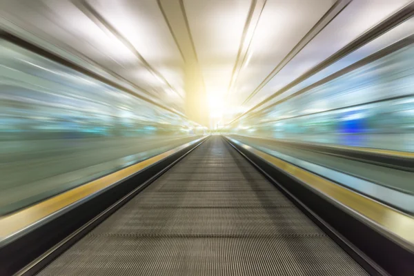 Perspective wide angle black and white view of modern light blue illuminated and spacious high-speed moving escalator with fast blurred trail of handrail in vanishing traffic motion — Stock Photo, Image