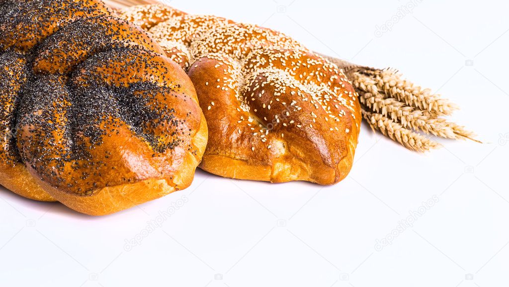 Two whole fresh challah bread with poppy and sesame seeds on a w