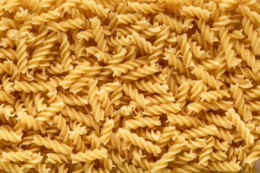 Kuru makarna fusili. Fusilli 'nin spiral şekli ve sarı rengi var. Makarna, erişte gibi buğday unundan yapılan İtalyan geleneksel makarnasıdır. Makarna arka planda.