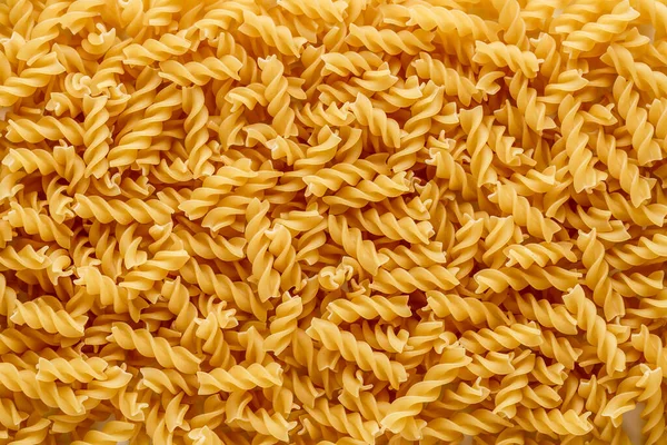Kuru makarna fusili. Fusilli 'nin spiral şekli ve sarı rengi var. Makarna, erişte gibi buğday unundan yapılan İtalyan geleneksel makarnasıdır. Makarna arka planda.