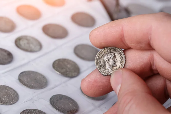 Numismatics. Old collectible coins made of silver on a wooden table. A collector holds an old coin.Ancient coin of the Roman Empire.
