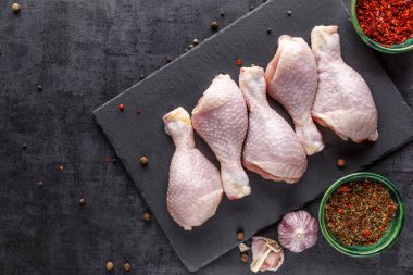 Katalog için çekim yapıyorum. Tahta bir tahtanın üzerinde baharatlı ve sebzeli çiğ tavuk bacağı. Siyah arka plan. Üst görünüm