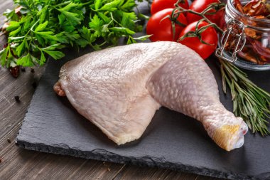 Katalog için çekim yapıyorum. Tahta bir tahtanın üzerinde baharatlı ve sebzeli çiğ tavuk bacağı. Siyah arka plan. Üst görünüm