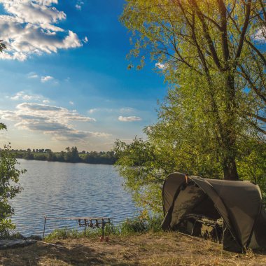 Balıkçılık maceraları, sazan avcılığı. Balıkçı gün batımında balık tutma tekniğiyle balık tutar. Gölün kıyısında kamp. Sazan Balıkçılık Günbatımı.