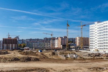 İnşaat alanı geçmişi. Vinç kaldırma ve yeni çok katlı binalar. Endüstriyel arka plan. İnşaat alanı mavi gökyüzüne karşı çalışıyor.