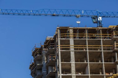 Yeni bir apartman bloğunda çalışma platformları sağlayan geniş kapsamlı yapı iskeleleri, inşaat halindeki uzun binalar, bir inşaat sahasındaki serbest kule vinci.