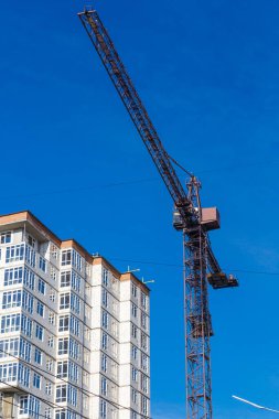 Yeni bir apartman bloğunda çalışma platformları sağlayan geniş kapsamlı yapı iskeleleri, inşaat halindeki uzun binalar, bir inşaat sahasındaki serbest kule vinci.